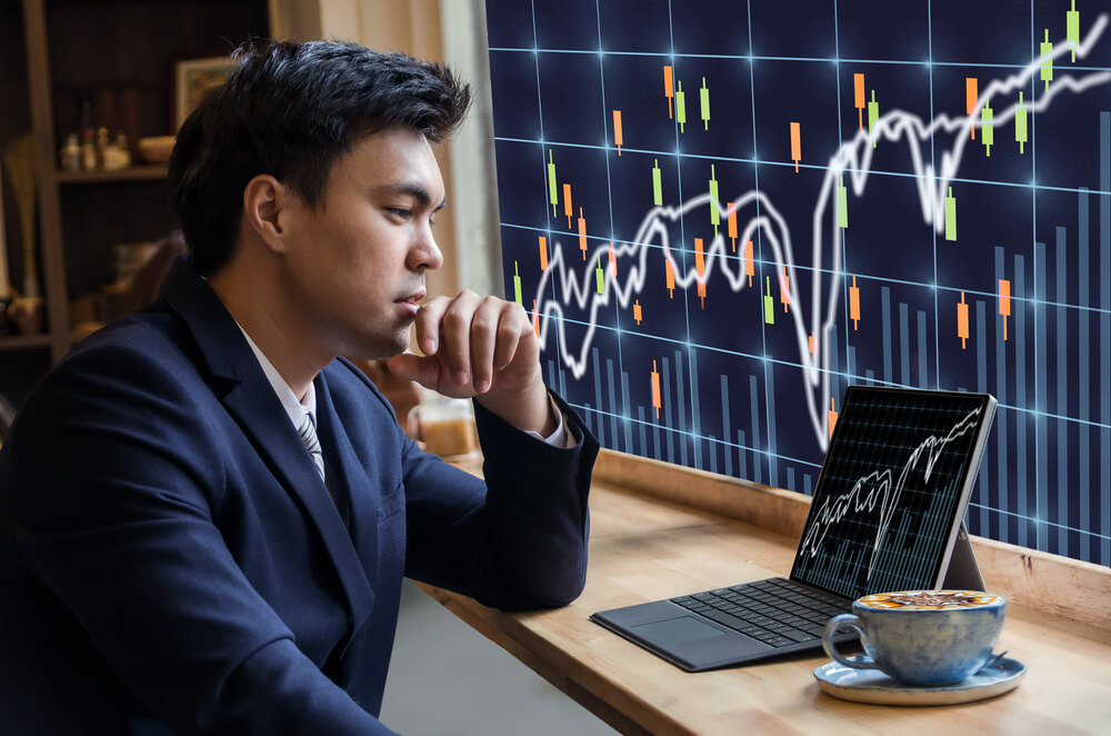 Asian Businessman sitting and using computer laptop showing trading graph